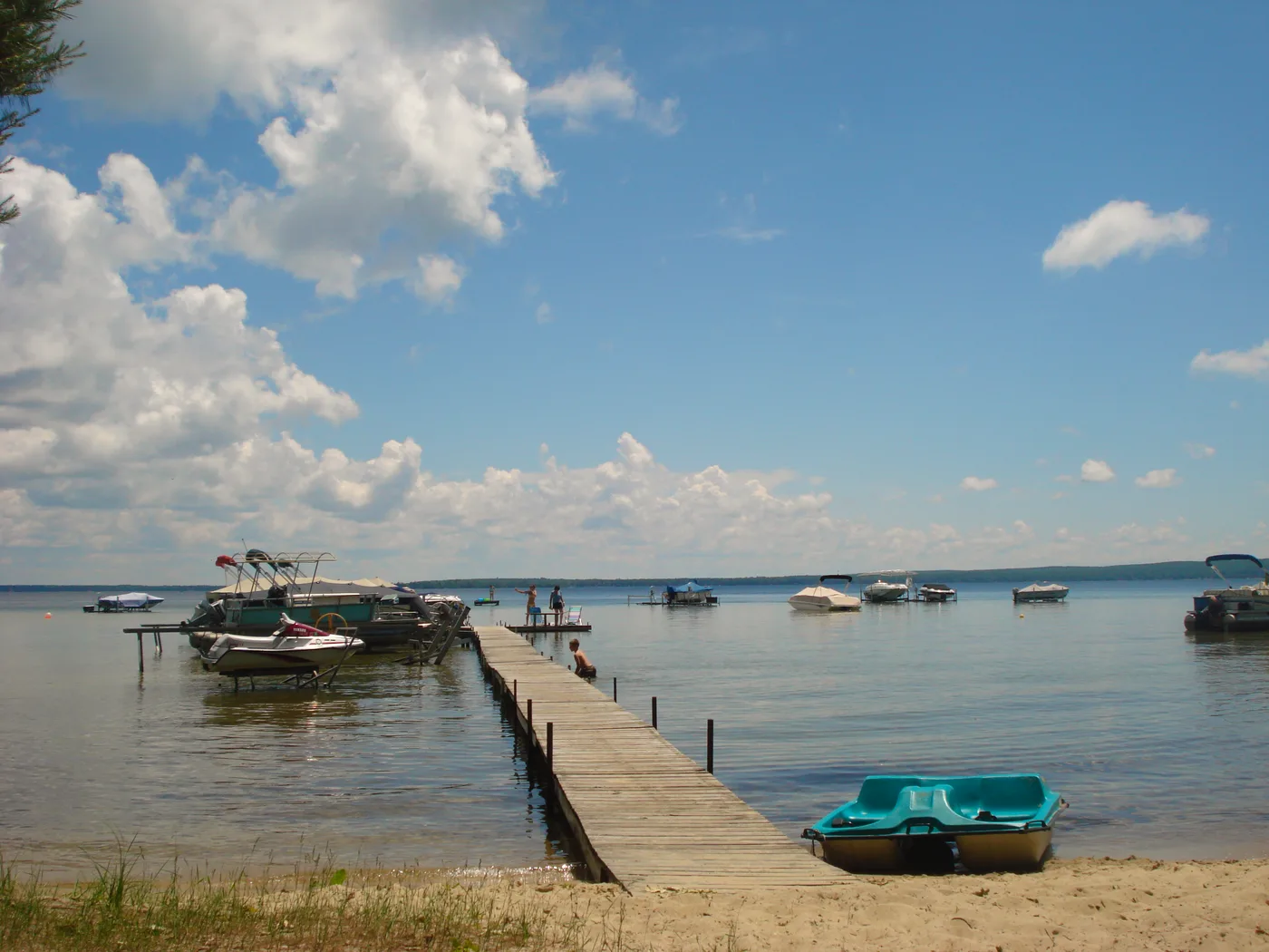 Sandy beach, dock and pontoon boats on the clear blue water of Higgins Lake, Michigan
