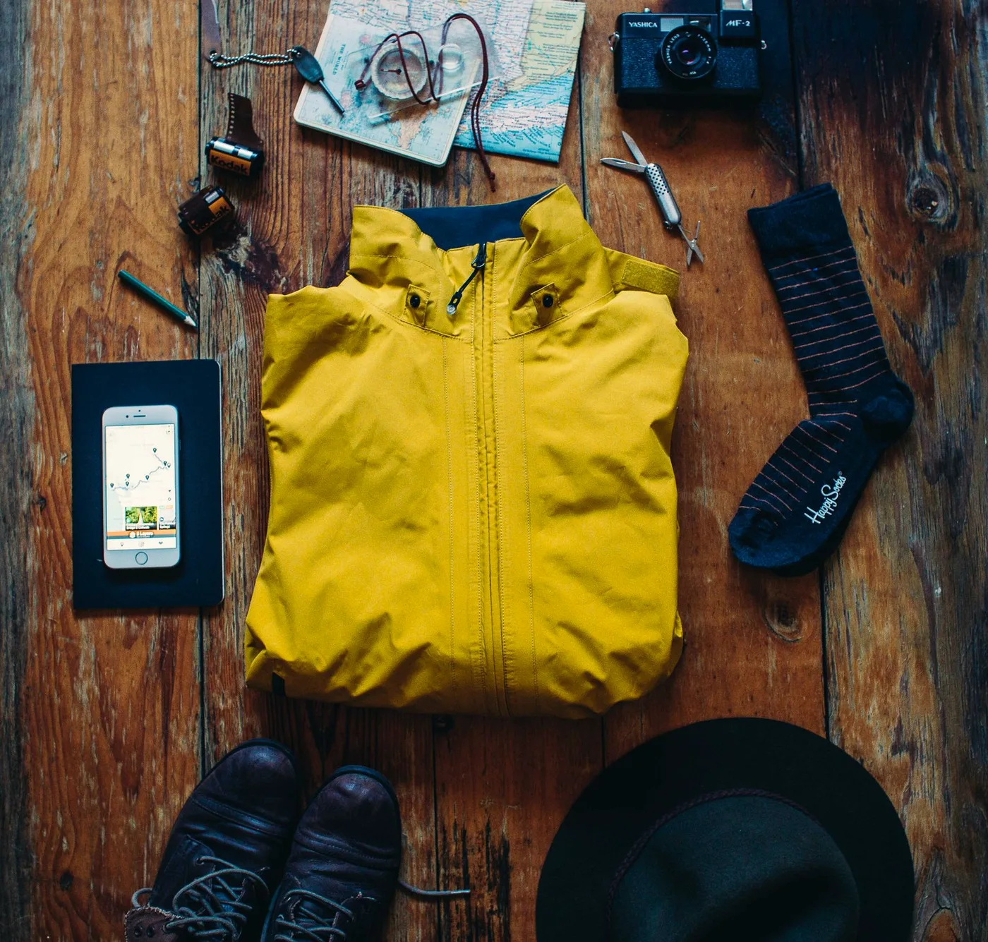 Flat lay of day-hike essentials: jacket, map, boots, water and camera
